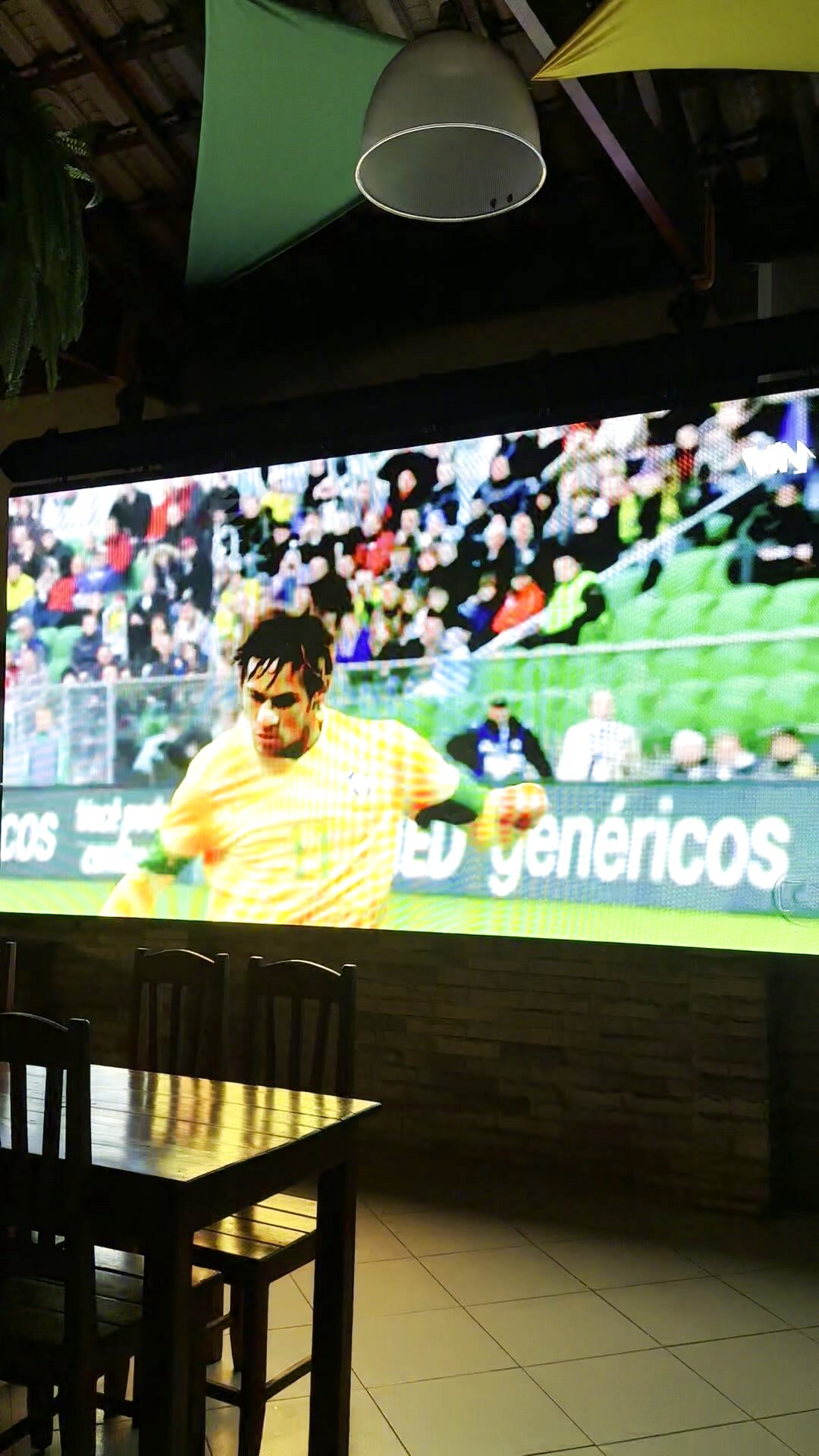 Interior da Kabana com mesas de madeira e telão ao fundo